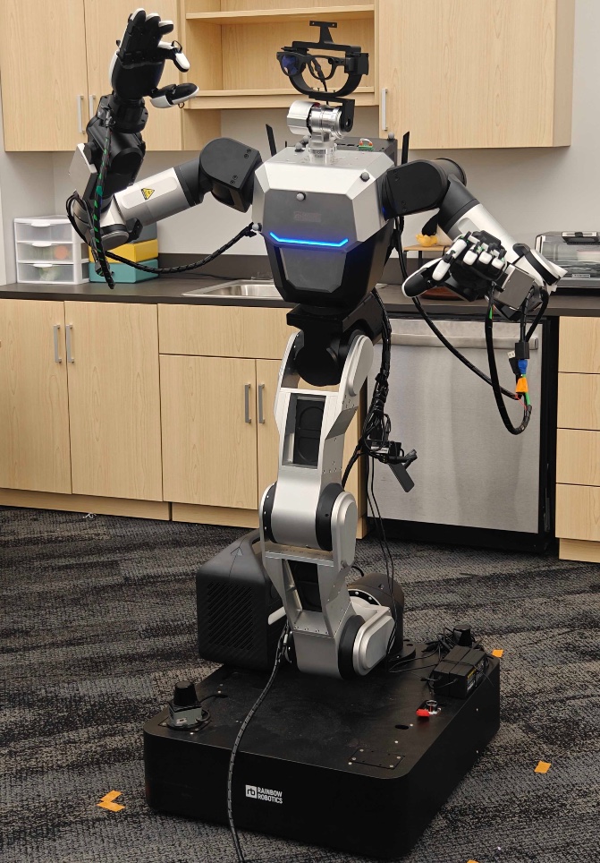 The RB-Y1 wheeled humanoid in a kitchen: two arms with five-fingered hands, a head carrying Project Aria glasses, a segmented torso, and a black mobile base.